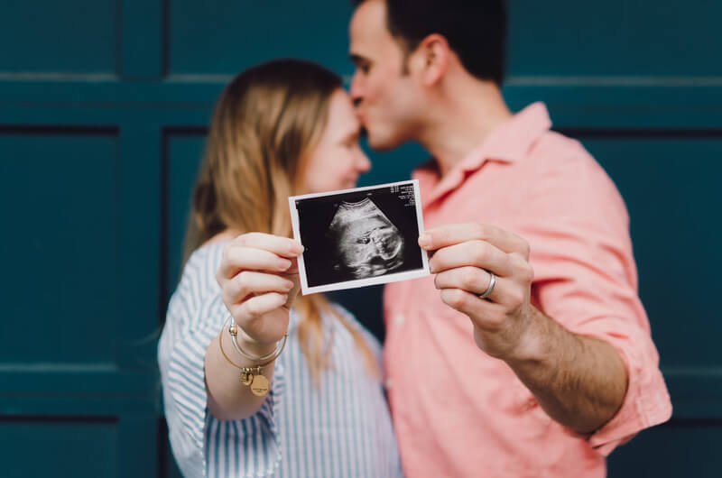 a happy couple kissing and holding up a baby ultrasound image